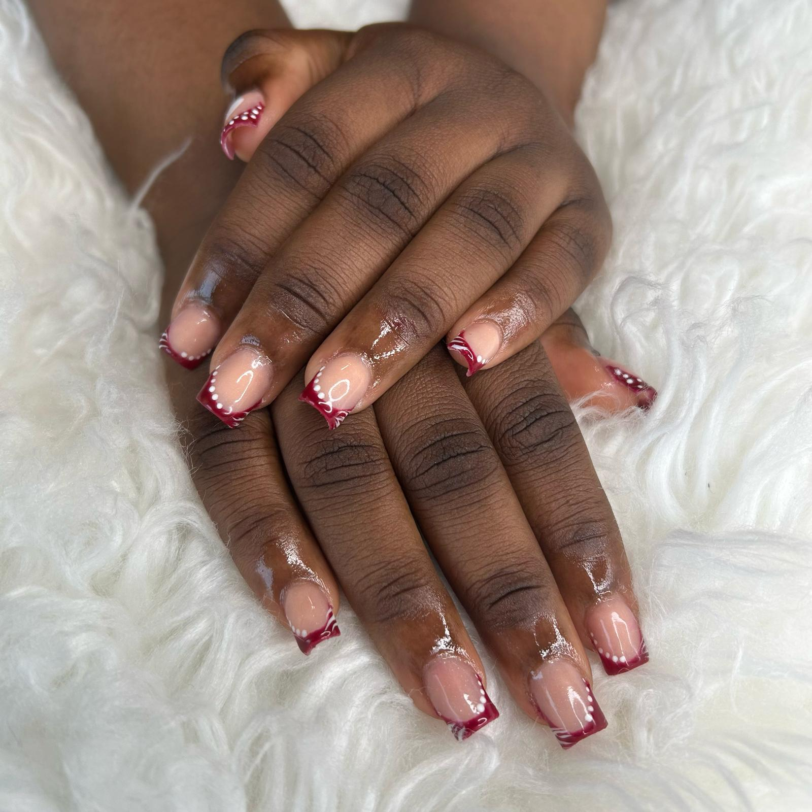 Burgundy French tips with white swirls and pearl dots.