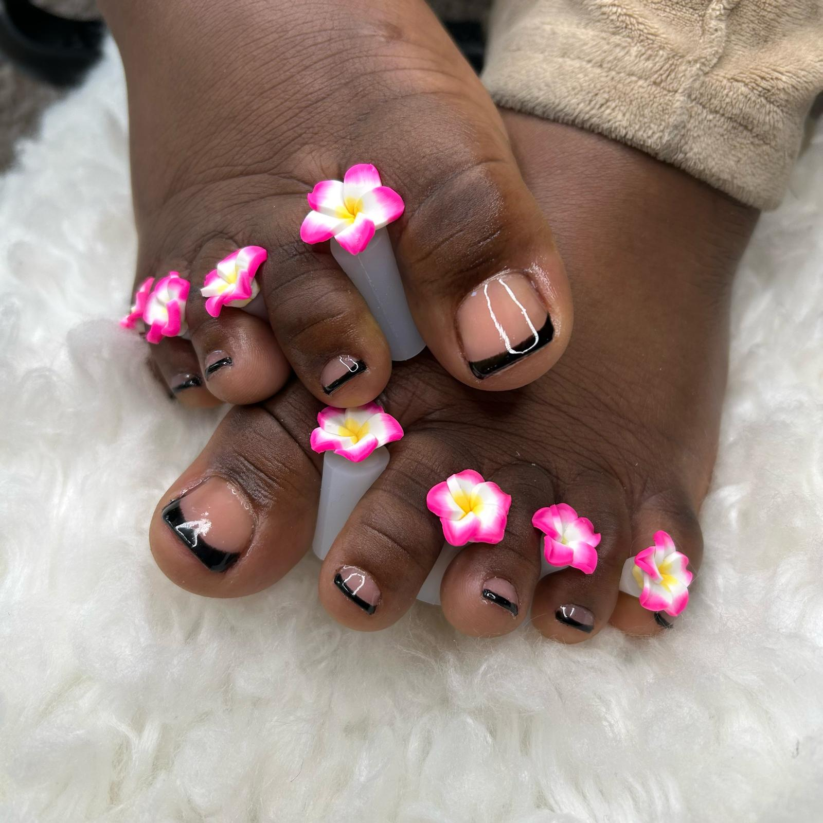 Black French pedicure with pink frangipani toe accents.